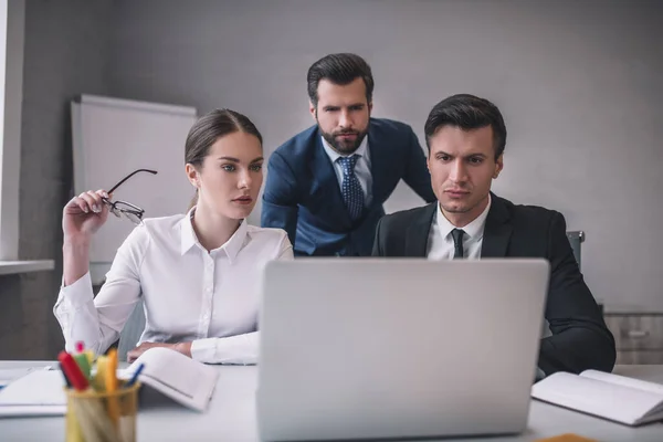 Frau und zwei Männer blicken auf Laptop-Bildschirm — Stockfoto