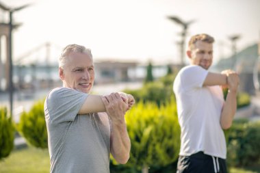 Genç sakallı erkek ve olgun gri saçlı erkek dışarıda kollarını uzatıyor.