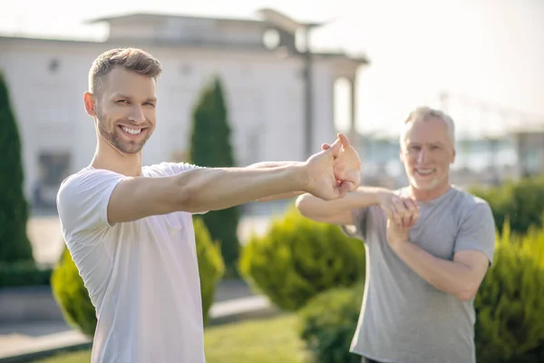 Bearded male and mature grey-haired male stretching hands outside, smiling — Stock Photo, Image