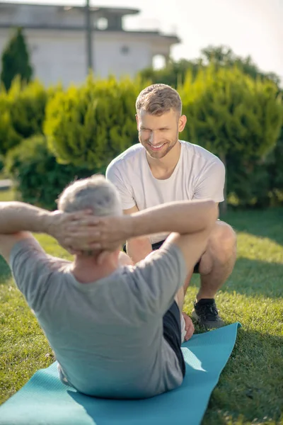 Leende brunhårig man som hjälper gråhårig man med sit ups — Stockfoto
