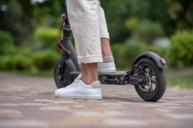 Scooter 'ın üstünde duran insan ayaklarının resmini kapat.