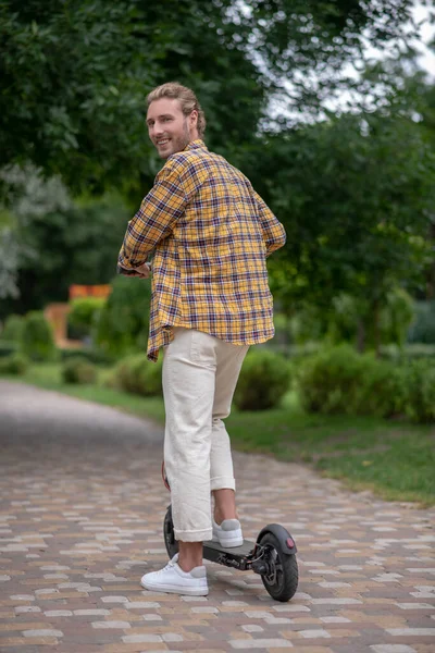 A man in checkered shirt riding a scooter in the park — Stock Photo, Image