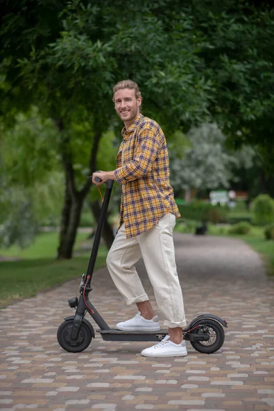 Bonito jovem montando uma scooter e sorrindo — Fotografia de Stock