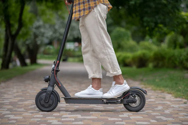 Egy férfi áll egy robogón a parkban. — Stock Fotó