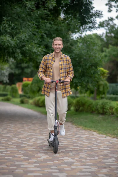 Schöner junger Mann fährt Roller im Park und fühlt sich wohl — Stockfoto