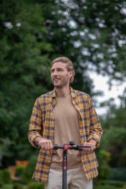 Beyaz pantolonlu bir adam motosiklet sürüyor ve yana bakıyor.