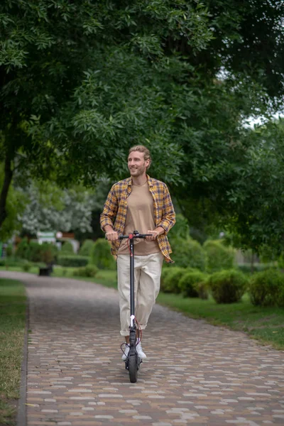 Homem de calças brancas montando uma scooter push no parque — Fotografia de Stock