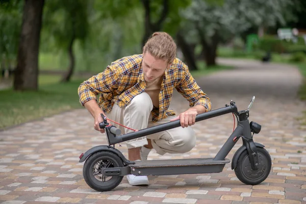 Man in checkered shirt looking involved while fixing push scooter — Stock Photo, Image