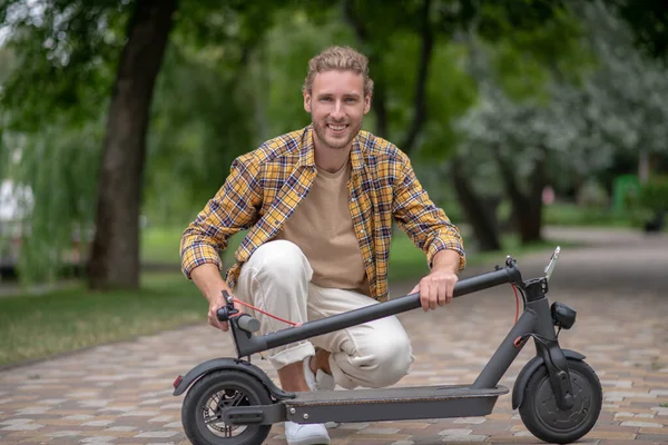 Man in checkered shirt holding scooter and looking cheerful — Stock Photo, Image