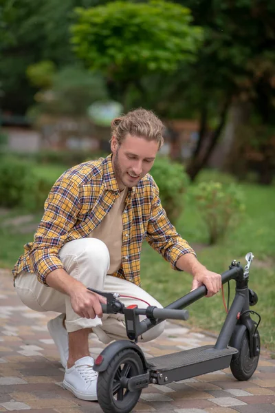 Мужчина в клетчатой рубашке выглядит вовлеченным, пока чинит свой скутер — стоковое фото