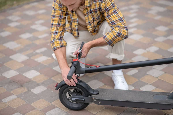 Giovane seduto sui suoi hunkers e fissare il suo scooter — Foto Stock