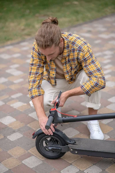 Uomo seduto sui suoi hunkers e regolando il suo scooter — Foto Stock