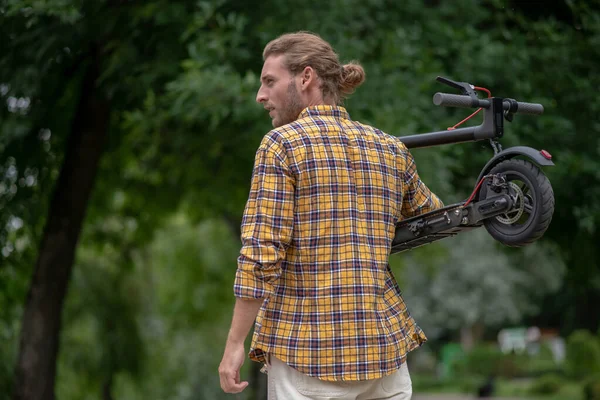 Mann im karierten Hemd trägt Roller und schaut zur Seite — Stockfoto