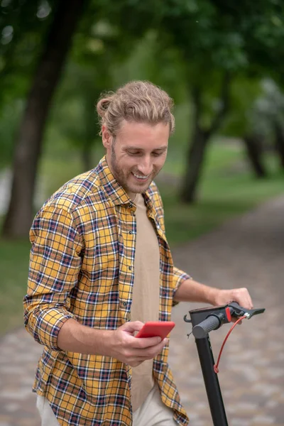 Человек со скутером, который пишет смс и улыбается. — стоковое фото