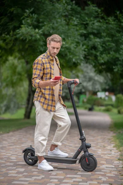 Homem de camisa quadriculada apoiado em sua scooter e mensagens de texto — Fotografia de Stock