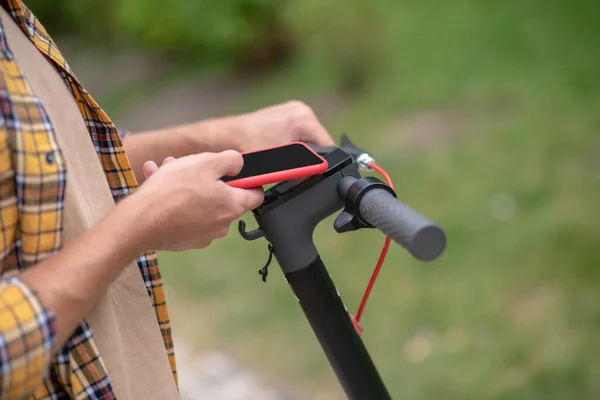 Homem segurando um telefone e se conectando com configurações de scooter — Fotografia de Stock