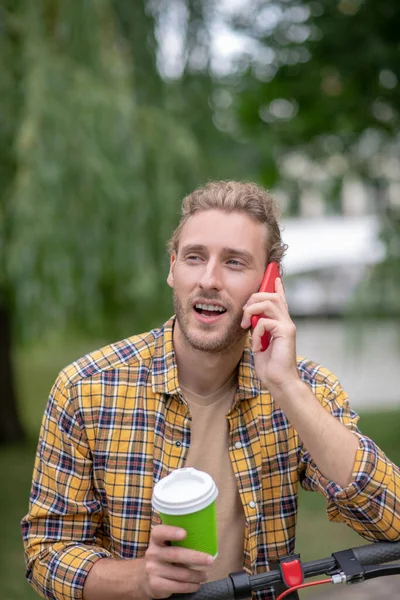 Sarışın, yakışıklı bir adam elinde kahve fincanıyla telefonda konuşuyor. — Stok fotoğraf