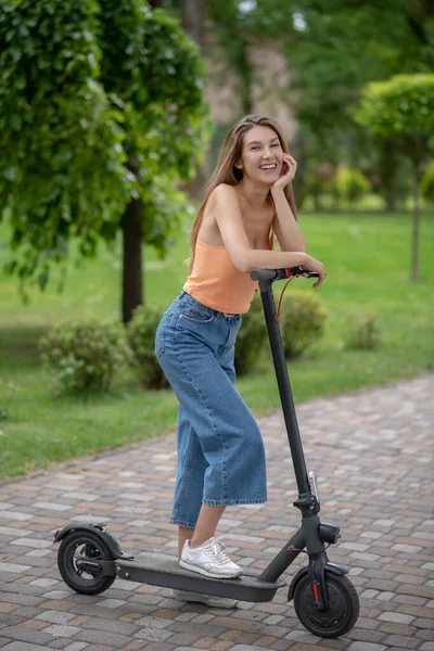 Langharig schattig meisje rusten op haar scooter en glimlachen — Stockfoto