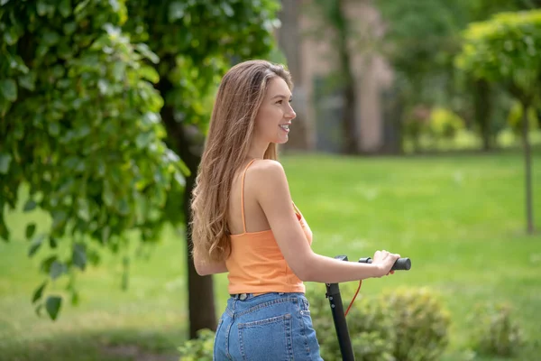 Chica de pelo largo disfrutando de montar una scooter en el parque —  Fotos de Stock