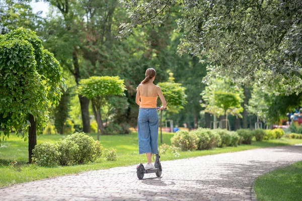 Narancssárga felsős lány robogózik a parkban — Stock Fotó