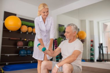 Sarışın terapist, erkek hastaya antrenman sırasında yardım ediyor.