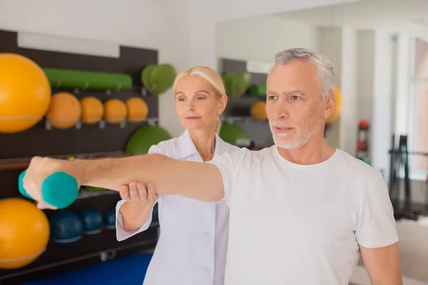 Blond fysiotherapeut assisteren van een mannelijke patiënt tijdens de training — Stockfoto