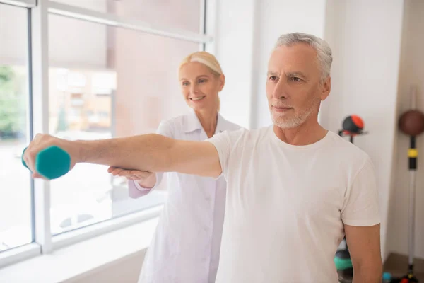 Blond leende terapeut hjälpa en manlig patient under träningen — Stockfoto