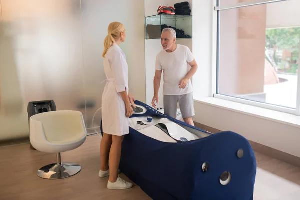 Paciente masculino de pelo gris que habla con el médico en la sala de procedimientos en el centro de rehabilitación — Foto de Stock