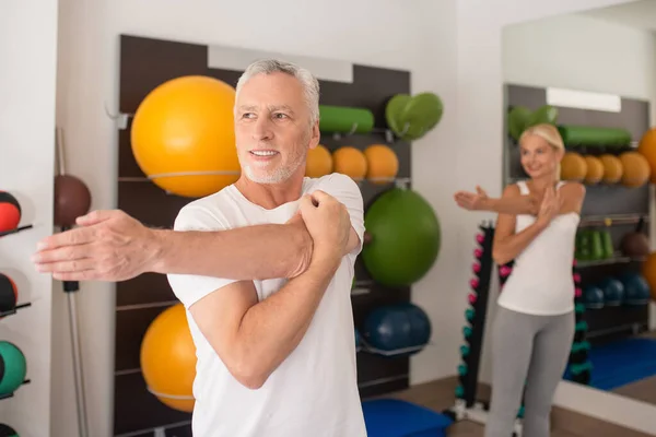 Um homem e uma mulher esticando os braços na aula de fitness e olhando contente — Fotografia de Stock