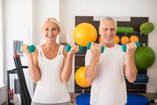 Hombre y mujer positivos haciendo ejercicio con pesas en el gimnasio — Foto de Stock