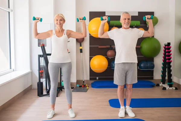 Pozitif erkek ve kadın dambıllarıyla egzersiz yapıyor ve kollarını kaldırıyor. — Stok fotoğraf