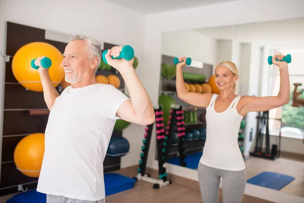 Hombre y mujer maduros haciendo ejercicio con mancuernas y levantando los brazos — Foto de Stock