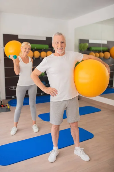 Homem com uma bola e uma mulher com halteres exercitando juntos no ginásio — Fotografia de Stock