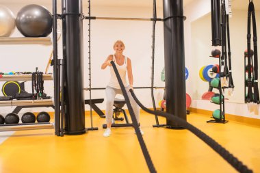 Spor kıyafetli sarışın kadın spor salonunda ipleri çekiyor.