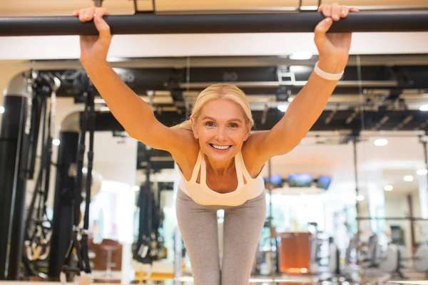 Женщина наклоняется вперед делая упражнения в тренажерном зале и улыбаясь — стоковое фото
