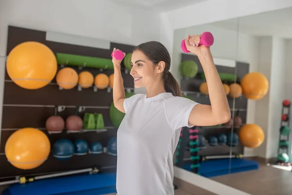 Sonriente hembra morena haciendo ejercicio con pesas en el gimnasio — Foto de Stock