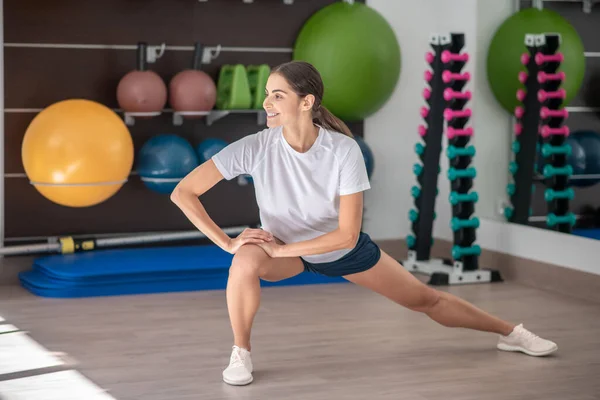 Sonriente hembra morena estirando las piernas, las manos en la rodilla derecha — Foto de Stock