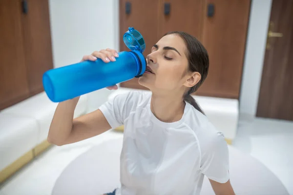 Mujer morena sentada en el vestuario, bebiendo agua — Foto de Stock