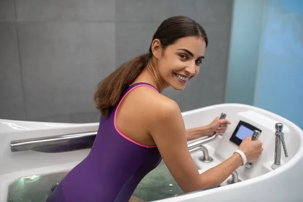 Улыбающаяся темноволосая женщина в фиолетовом плавании расслабляется в гидромассажной ванне — стоковое фото