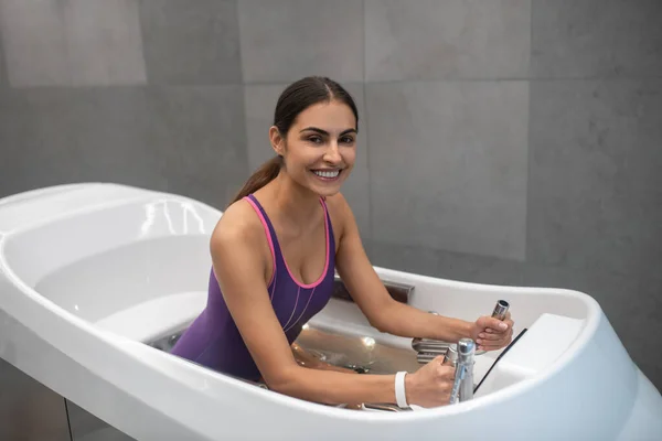 Счастливая темноволосая женщина в фиолетовом купальнике получает гидротерапию — стоковое фото