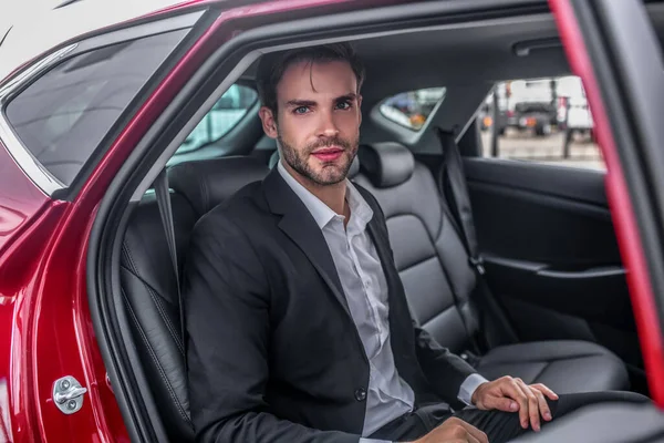 Brown-haired male sitting at backseat of red car — Stock Photo, Image