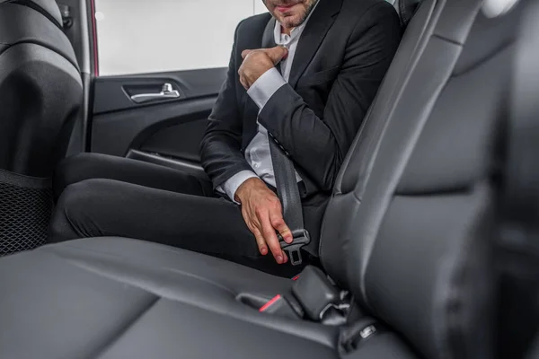 Hombre sentado en el asiento trasero del coche, abrochándose el cinturón de seguridad —  Fotos de Stock
