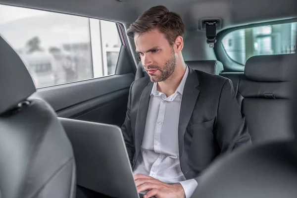 Brown-haired male sitting at backseat of car, working on laptop — Stock Photo, Image