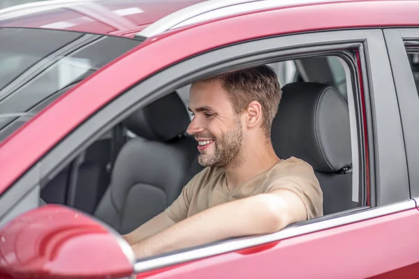 Leende ung man kör röd bil, sätta armbåge ut genom fönstret — Stockfoto