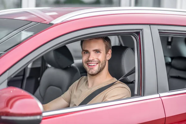 Uśmiechnięty brodaty młody mężczyzna prowadzący czerwony samochód — Zdjęcie stockowe