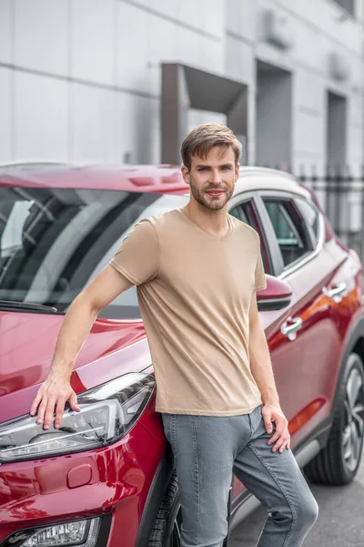 Usmívající se mladý muž opírající se o červené auto venku — Stock fotografie
