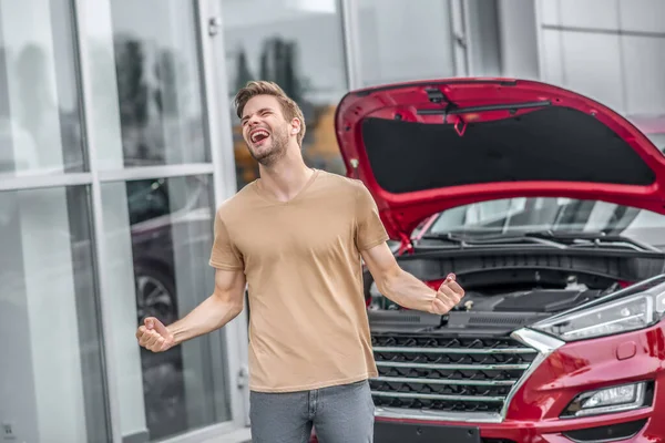 Autista maschio urla, stringendo i pugni di fronte a una macchina rotta con cappuccio aperto — Foto Stock
