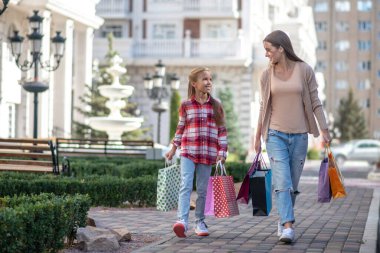 Anne ve kızı alışveriş torbalarıyla sokakta yürüyorlar.