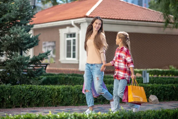 Mutlu anne ve kız alışveriş torbalarıyla el ele yürüyorlar. — Stok fotoğraf