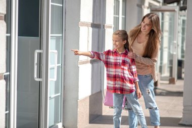 Gülümseyen anne, kızını kucaklıyor ve kapıyı işaret ediyor.